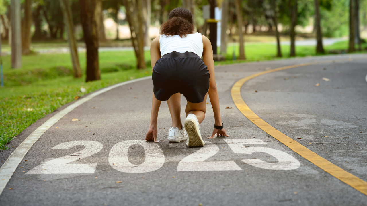 Woman reaching her fitness resolution by running on a track with 2025 chalked.